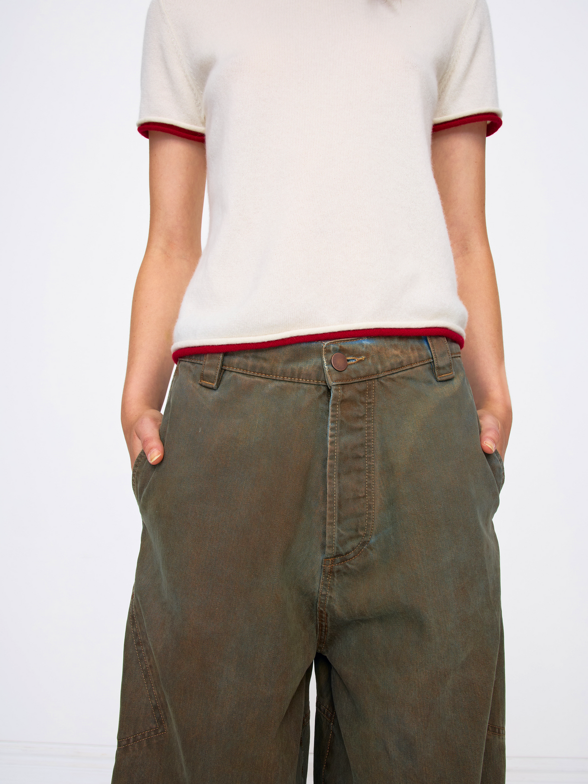 A person wearing a cream short-sleeve ringer T-shirt with red trim and olive green wide-leg pants, shown from the chest down against a plain white studio background.