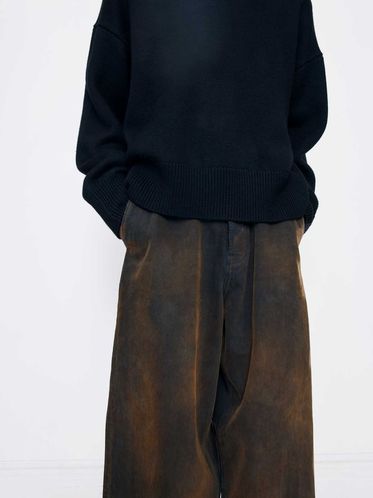 A person shown from the back wearing a black knit sweater and dark brown wide-leg pleated trousers against a plain white background.