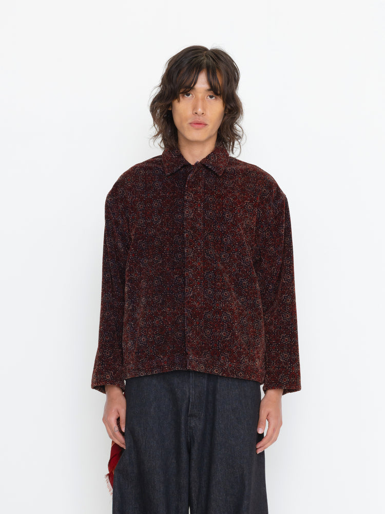 Person wearing a patterned shirt and dark pants on a white background