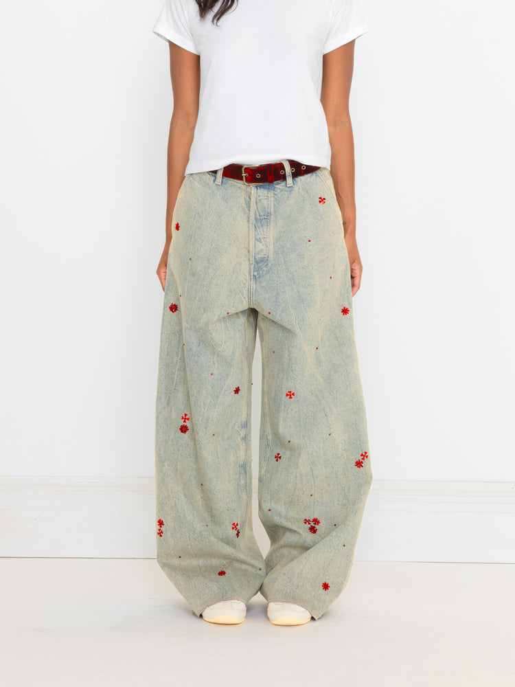Person wearing light blue jeans with red floral patterns on a white background