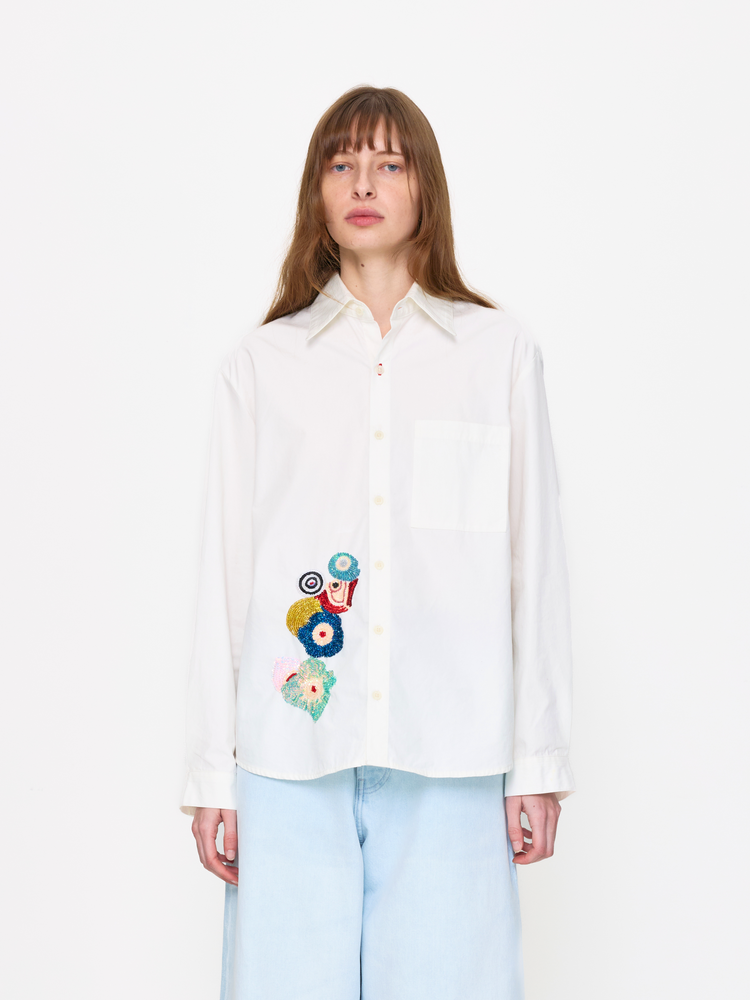 Woman wearing a white blouse with colorful floral embroidery on a white background