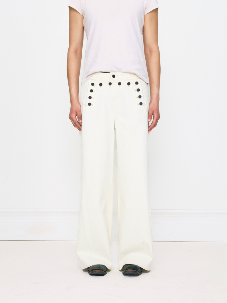 Person wearing white pants with black button details on a white background