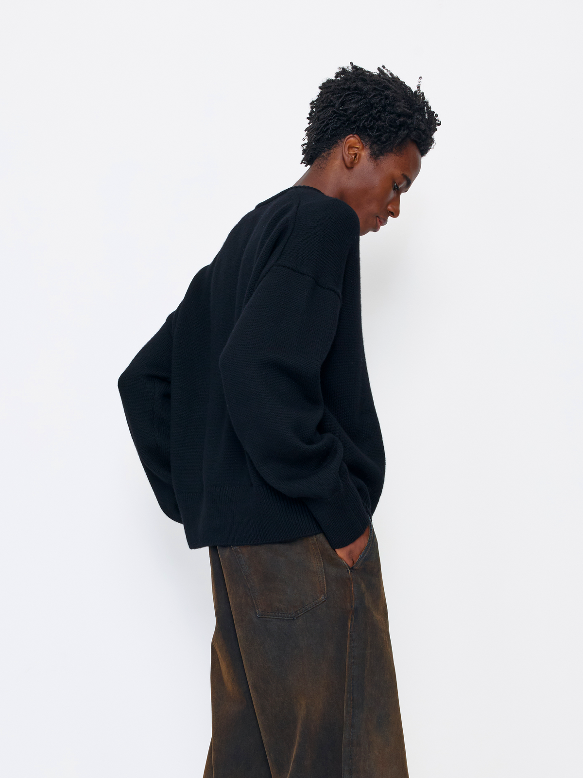 A model wearing a black oversized crewneck sweatshirt and brown wide-leg corduroy pants, shown from a side-back angle against a plain white studio background.